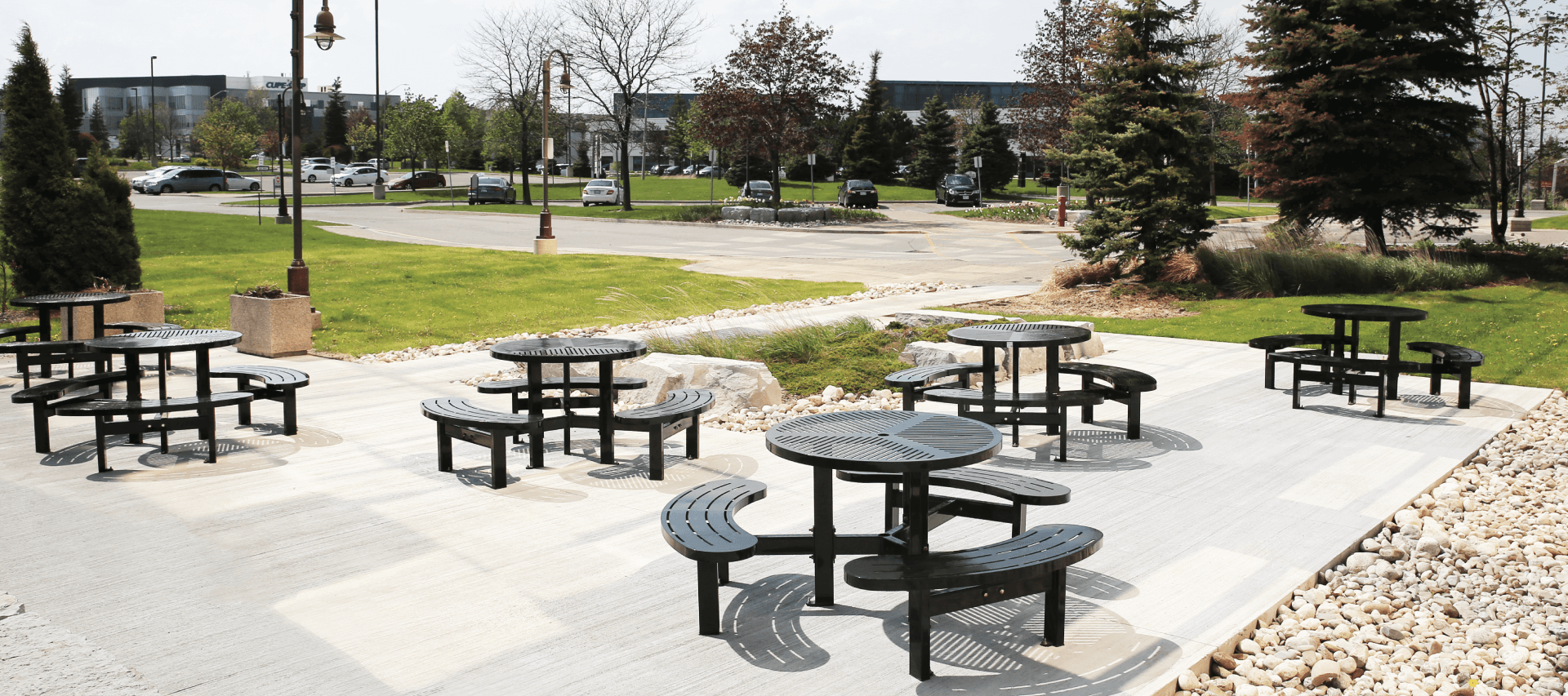 5 round shaped steel commercial picnic tables outside an office building